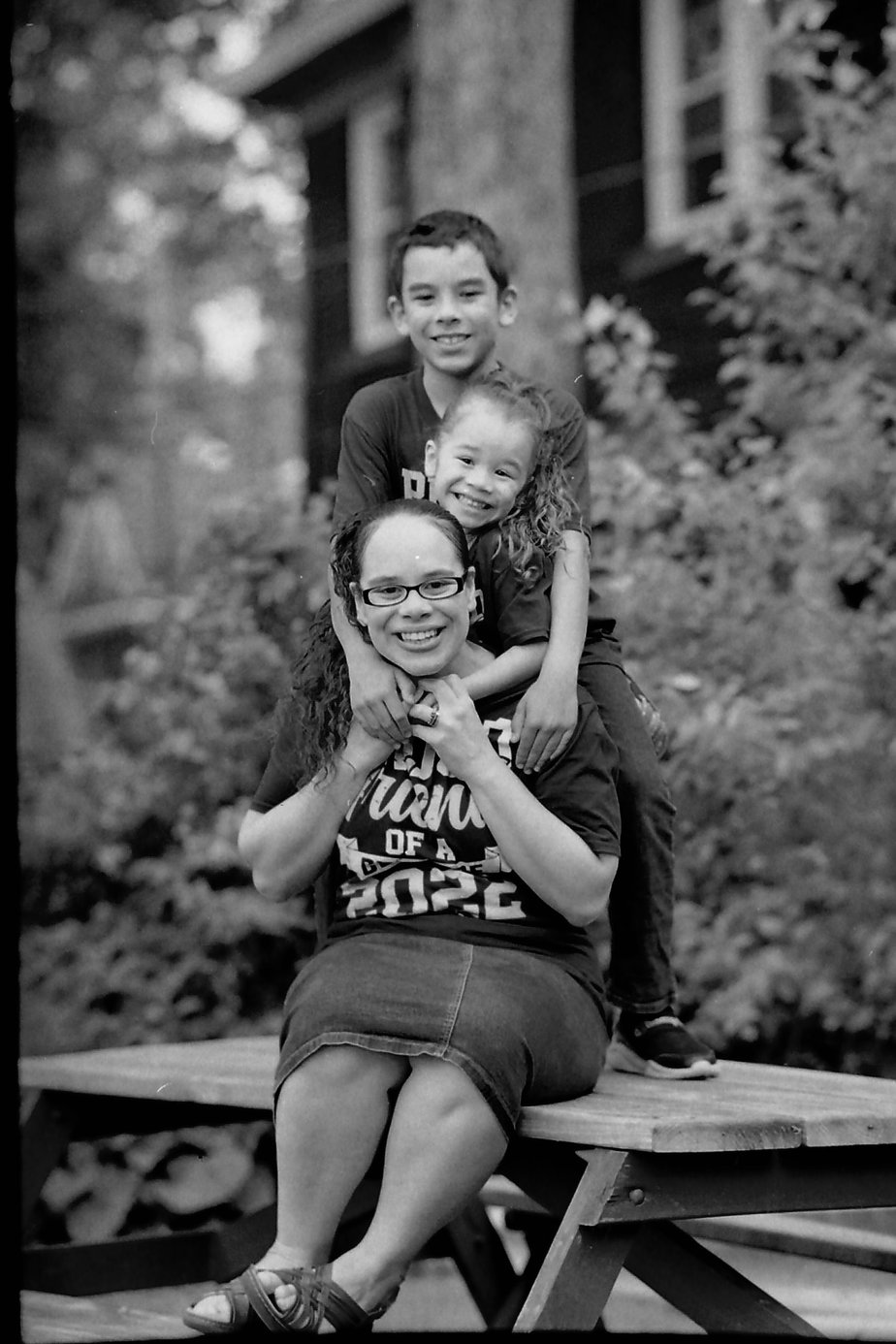 Yessi with her two children joyfully smiling while sitting on a picnic table