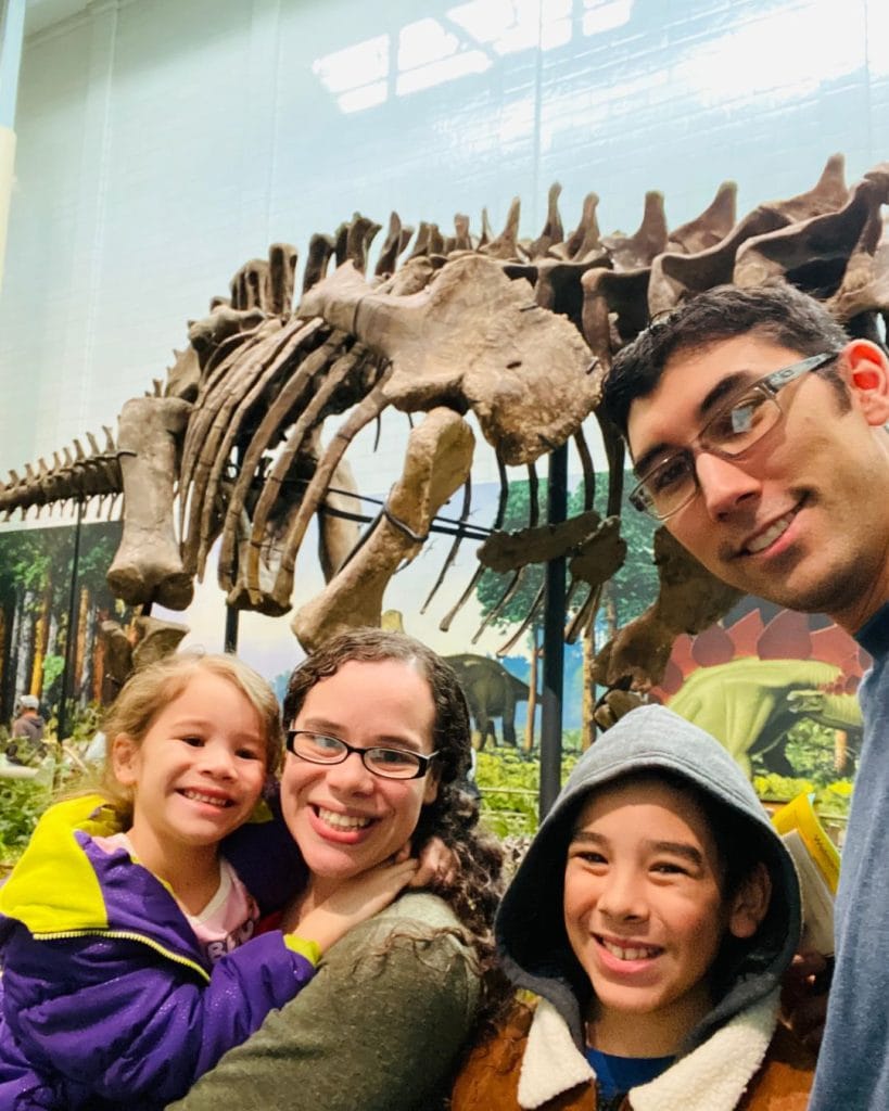 Picture of Yessi and her family at the Carnegie Museum with a dinosaur fossil behind them