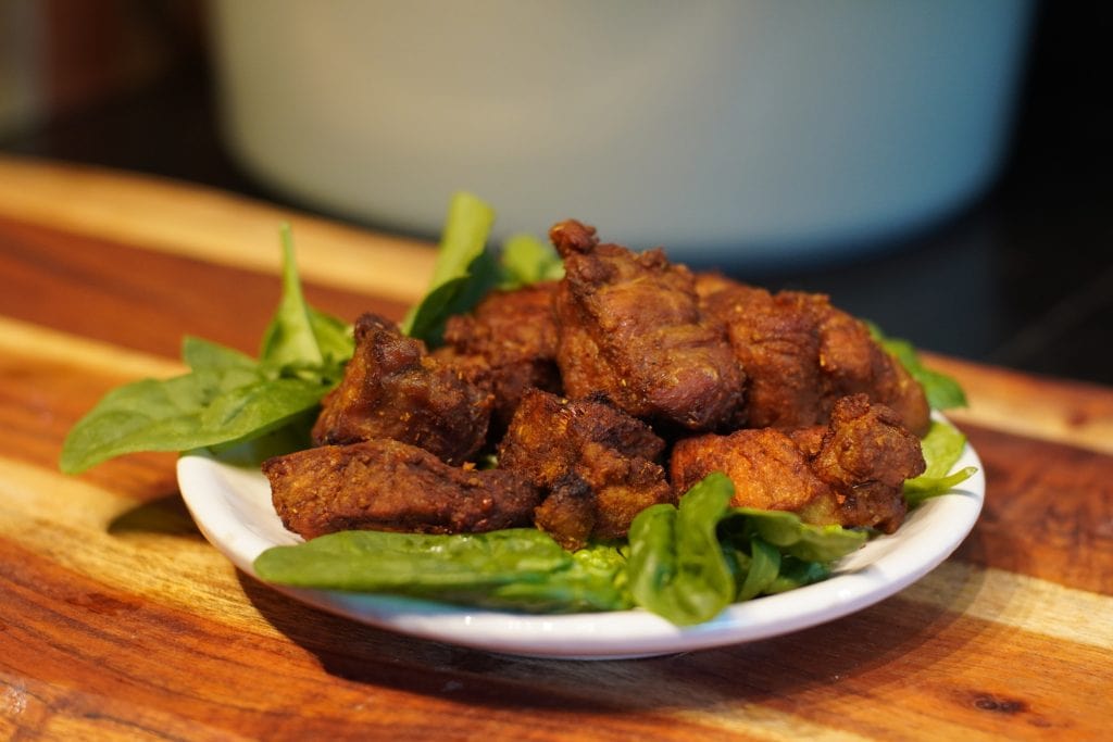 Pieces of carne frith served over some greens on a white dish with
