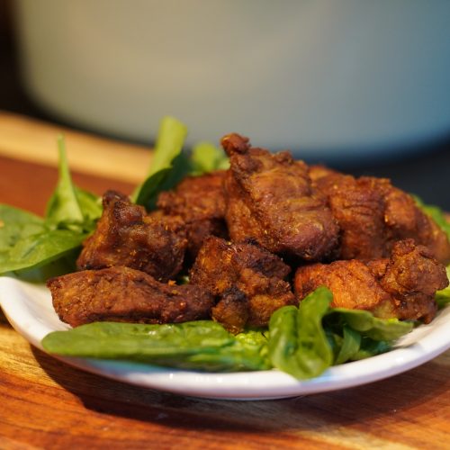 Pieces of carne frith served over some greens on a white dish with