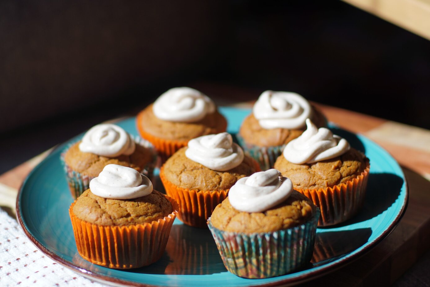 7 gluten-free pumpkin muffins topped with a cinnamon cream cheese topic place on a round teal plate