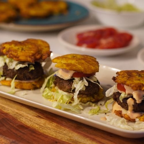 3 Puerto rican jibarito sliders on a square plate with a wooden cutting board underneath